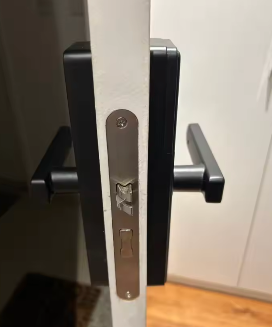 Open door edge showing the latch and both lever handles of the black smart door lock