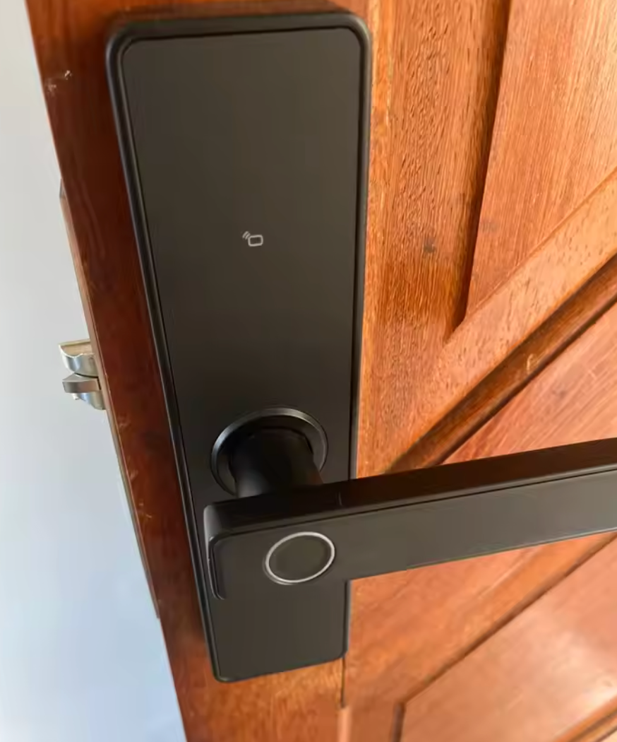 Black lever-handle smart door lock fitted to a dark timber entry door