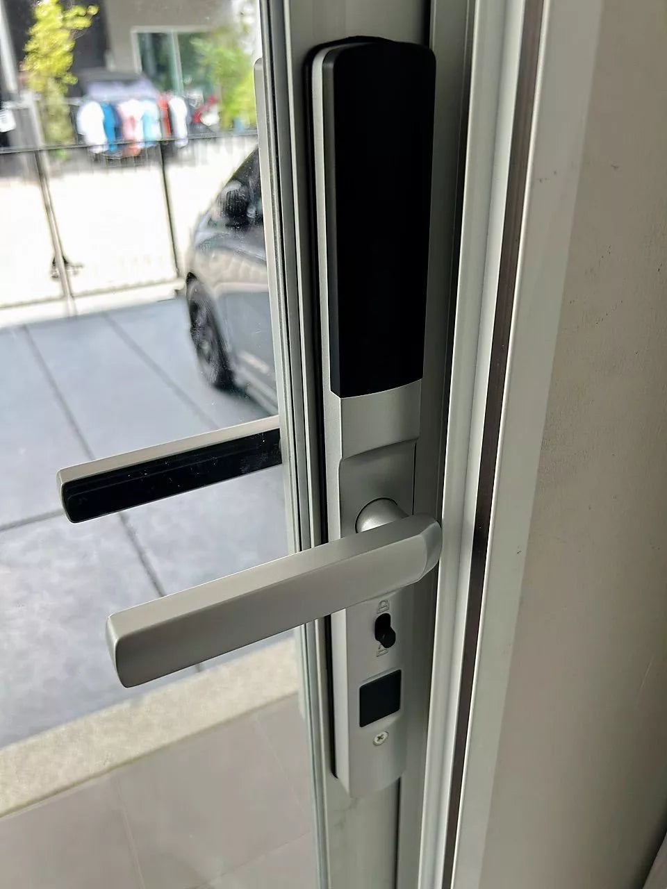 Silver smart door lock on a glazed door, looking out to a paved driveway